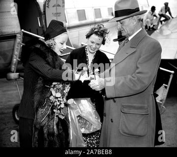 Senator William Gibbs McAdoo, von Kalifornien, um die Beihilfe von Fräulein Marion Weldon, Paramount starlet, als sie für ihre Schönheit aids Vor dem Grußwort throng bei Ihrer Ankunft am Flughafen in Washington heute sucht. Stockfoto