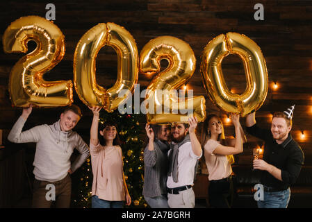 Drei junge glückliche Paare halten aufblasbare Folie Zahlen 2020 Stockfoto