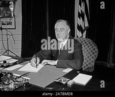 Präsident Franklin Roosevelt sitzen an einem Schreibtisch und Unterzeichnung ein Stück Papier Ca. 1934 Stockfoto