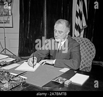 Präsident Franklin Roosevelt sitzen an einem Schreibtisch und Unterzeichnung ein Stück Papier Ca. 1934 Stockfoto