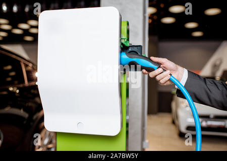 Mann stecken das Kabel in die Ladestation für Elektroautos im Autohaus, Nahaufnahme Stockfoto