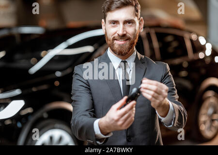 Porträt eines eleganten Verkäufer mit einem Autoschlüssel, Verkauf von Elektrofahrzeugen im Autohaus Stockfoto
