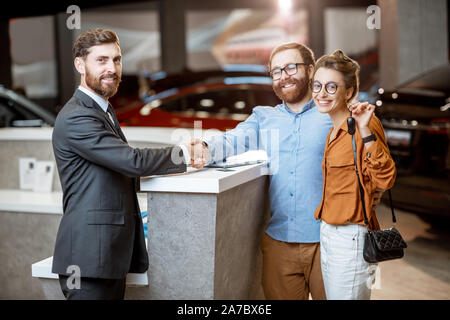 Porträt von einem Sales Manager die Hände schütteln mit einem glücklichen Käufer im Autohaus. Junges Paar kaufen New Electric Car Stockfoto