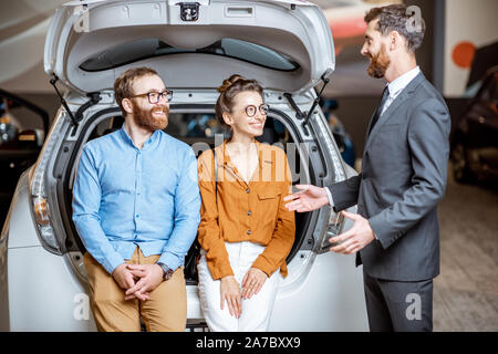 Junges Paar Hören des Sales Consultant, sitzt im Kofferraum im Autohaus Stockfoto