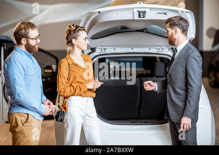Sales Manager mit geräumigen Kofferraum für ein junges Paar im Autohaus Stockfoto