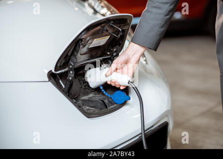 Mann stecken Ladekabel in die Kfz-Buchse, close-up. Elektroauto aufladen Konzept Stockfoto