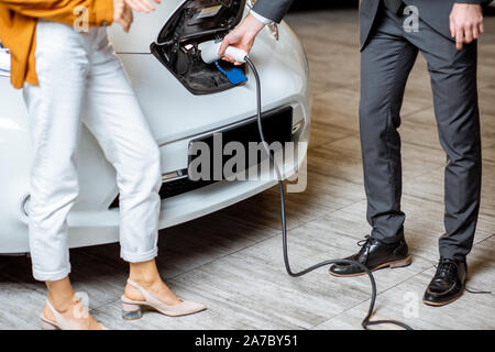 Sales Manager zeigt, wie elektrisches Auto zu einem jungen Client aufzuladen, schließen Sie Kabel in die Kfz-Buchse im Autohaus. Nahaufnahme mit kein Gesicht Stockfoto