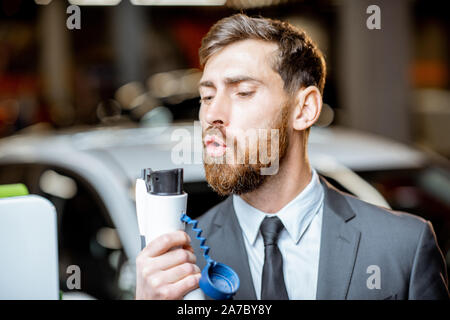 Lustige Portrait von einem sales manager Holding laden Pistole wie eine Pistole, Verkauf von Elektroautos im Showroom Stockfoto