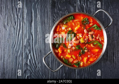 Italienische borlotti oder cranberry Bohnen Suppe mit Sellerie, Gemüse, Spinat, Parmesan und Tomaten in einen Topf auf einem schwarzen Holztisch, horizontale vie Stockfoto