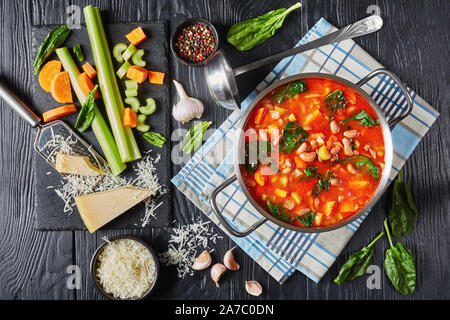 Cranberry Bohnen Suppe Spinat mit Parmesan und Tomaten in einer Pfanne auf einem schwarzen Holztisch, Zutaten auf einem schwarzen Stein, italienische Küche Stockfoto