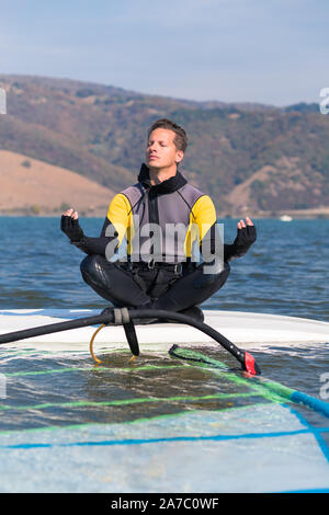 Mann in Anzug sitzen auf Surfen in Lotus Position und die Meditation Zen Übung. Windsurfen und Life Balance Konzept. Stockfoto