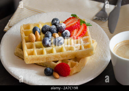 Nahaufnahme des Belgischen Waffeln dekoriert mit Erdbeeren, Blaubeeren, Mandeln und Puderzucker. . Köstliche hausgemachte Desserts zum Frühstück. Stockfoto