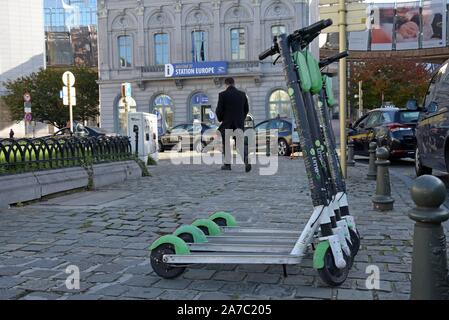 Eine Reihe von Kalk S dockless Elektrische mieten Roller in Place de Luxemburg, Brüssel mit dem Europäischen Parlament Gebäude im Hintergrund Stockfoto