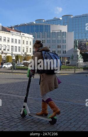 Eine Frau reitet auf einem Kalk elektrische mieten Roller in Place de Luxenbourg, Brüssel, mit dem Europäischen Parlament Gebäude im Hintergrund Stockfoto