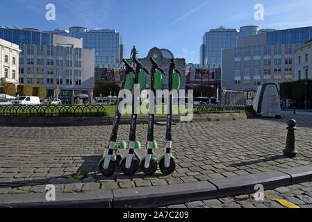 Eine Reihe von Kalk S dockless Elektrische mieten Roller in Place de Luxemburg, Brüssel mit dem Europäischen Parlament Gebäude im Hintergrund Stockfoto