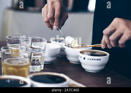 Professional Q Sortierer Vorbereitung zu testen und die Kontrolle der Qualität des Kaffees und der kaffeesatz aus Keramik Schale auf dem Tisch abschöpfen. Stockfoto