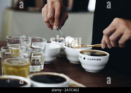 Professional Q Sortierer Vorbereitung zu testen und die Kontrolle der Qualität des Kaffees und der kaffeesatz aus Keramik Schale auf dem Tisch abschöpfen. Stockfoto