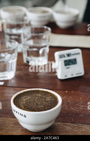 Kaffeesatz mit heißem Wasser in der Keramik Schale auf dem Tisch ist die Vorbereitung für die professionelle Q Sortierer für die Prüfung und die Kontrolle der Qualität des Kaffees. Stockfoto