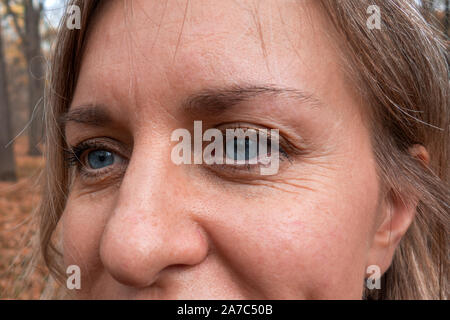 Nahaufnahme von Frau mittleren Alters mit blauen Augen. Echte Haut ohne Make-up und Korrektur. Sie nicht in die Kamera schauen. Lächelte Stockfoto