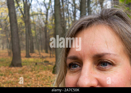 Gesicht Nahaufnahme von Frau mittleren Alters im Herbst Wald. Mädchen nicht an Kamera und lächelt auf unscharfen Hintergrund betrachten. Dachte, Meditation oder Zweifel expres Stockfoto