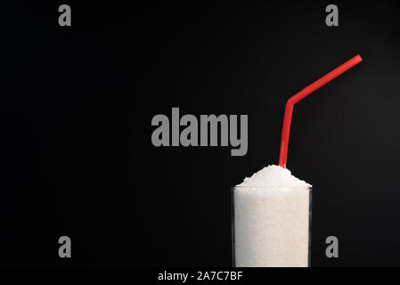 Ein Glas voll mit weißem Zucker mit Stroh auf schwarzem Hintergrund. Konzept der ungesunden Ernährung und diabetis Stockfoto