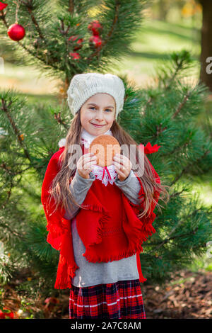 Süße Mädchen Essen Christmas cookies auf dem Hintergrund des Neuen Jahres Baum. Winterurlaub und Personen Konzept. Frohe Weihnachten und schöne Feiertage. Stockfoto