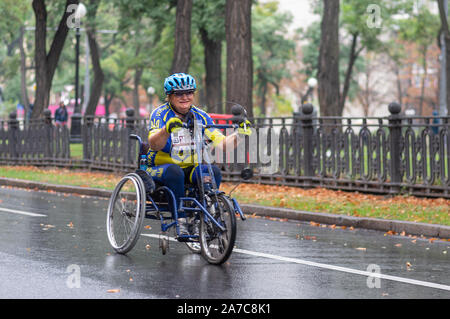 DNIPRO, UKRAINE - September 16, 2018: ältere Frau auf einem Stuhl an einem regnerischen city street während 10 km Abschnitt des ATB Dnipro Marathon Stockfoto