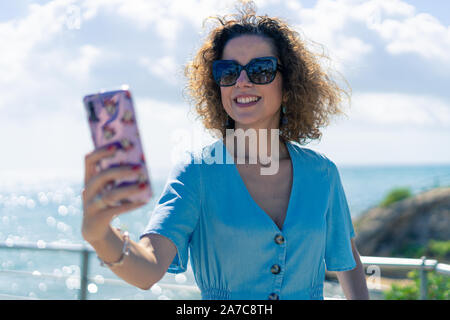 Touristische Frau im Sommerkleid und Sonnenbrille, eine selfie mit dem Smartphone. Stockfoto