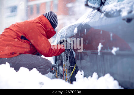 Schneeketten auf die Räder des Autos. Mann vorbereiten Auto im Winter schneebedeckten Tag reisen. Stockfoto