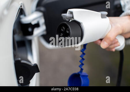 Nahaufnahme von Hand befestigen Sie das Netzkabel auf Umweltfreundliche Emissionsfreie Elektroauto Stockfoto