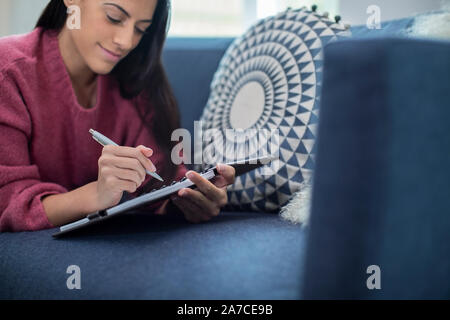 Junge Frau entspannt auf einem Sofa zu Hause Schreiben im Journal Stockfoto