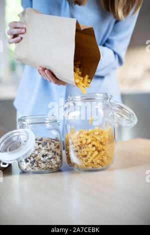 Nahaufnahme von Frau Gießen Pasta aus Kunststoff Free Packaging Paper Bag in Storage Jar Stockfoto