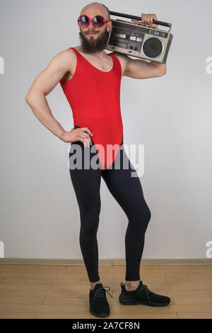 Ein Mann für Disco-retro Parteien gekleidet. Lustige bärtigen Kerl in der Sonnenbrille und leggings mit roten Strampler mit Retro tape recorder Stockfoto