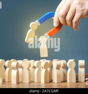 Geschäftsmann mit einem Magnet zieht Holzfiguren von Menschen aus der großen Masse. Die Einstellung von Arbeitnehmern. Suche erforderlich für Menschen und Arbeitnehmer mit der necessa Stockfoto