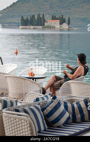 Ein Mann mit Blick auf das Wasser in Richtung UNSERER LIEBEN FRAU VON DEN FELSEN, eine kleine Insel, während er sich an einem Waterside Cafe trinken einen Kaffee am Morgen sitzen. Stockfoto