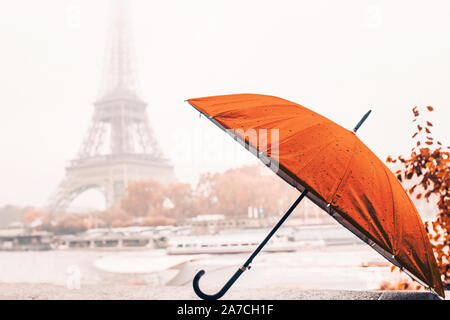 Helles orange Regenschirm an einem regnerischen Herbst nebligen Tag in Paris vor dem Hintergrund der Eiffelturm Stockfoto