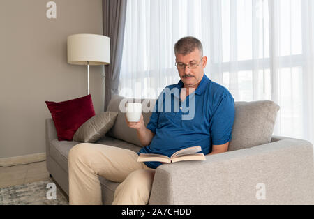 Im mittleren Alter Mann auf dem Sofa mit einem Buch Stockfoto