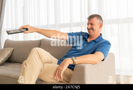 Im mittleren Alter Mann sitzt auf einem Sofa und Fernsehen Stockfoto