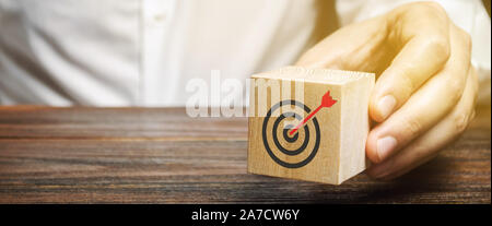 Ein Geschäftsmann hält in seinen Händen einen Holzklotz mit einer Ziel-Symbol. Das Konzept der Erreichung ihrer Ziele. Ausführung eines Business Plans. Purposefu Stockfoto