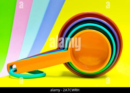 Kunststoff Messbecher mit verschiedenen hellen Farben gegen einen Multitouch-Bildschirm mit brillanten farbigen Hintergrund isoliert. Kunstvoll für Farbe pop angeordnet. Stockfoto