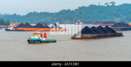 Der Verkehr von tugboat ziehen Lastkahn voller Steinkohle zu den Mahakam Fluss, Samarinda, Indonesien. Industrie und Bergbau Hintergrund Stockfoto