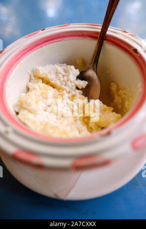 Frisch gekühlt Ricotta Salata und Honig in einem rustikalen Keramik Schüssel mit Löffel auf eine blaue Tischplatte - ricotta Käse Frühstück Dessert gemacht Stockfoto