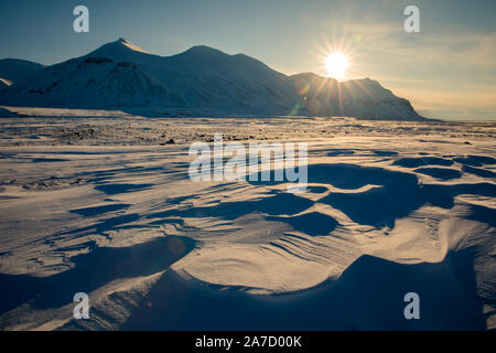 Arktischen Winterlandschaft an Kapp Ekholm, Steine im Vordergrund, mit Schnee bedeckten Bergen und blauen Himmel im Hintergrund. Hintergrundbeleuchtung, einem sonnigen Tag an Stockfoto