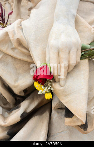 Rote Rose in der Hand auf Statue in den Friedhof gelegt. Stockfoto