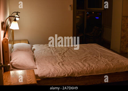 Bett in einem Hotel Zimmer. Das Bett und die Kissen. Ein Bett mit Kopfteil aus Holz und zwei Schränke und Stehlampen. Abend Hotel. Platz zum Schlafen und Entspannen. Stockfoto