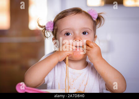 Adorable kleine Mädchen essen Spaghetti mit Sauce Bolognese mit ihren Händen. Säuglingsnahrung Stockfoto