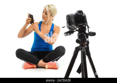 Der junge sportliche Mädchen mit blondem Haar sitzt vor der Kamera und zeigt Telefon Stockfoto