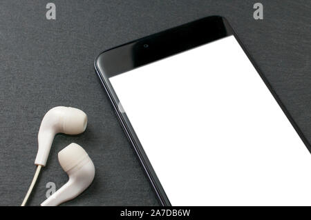 Leerer Bildschirm Smartphone auf Tisch aus Stein mit einer Reihe von weißen Ohrhörer Stockfoto