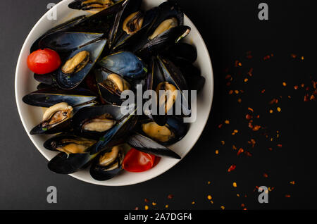 Italienisch Meeresfrüchte Delikatesse. Miesmuschel Suppe in Wein mit Tomaten und Peperoni auf schwarzem Hintergrund gedämpft. Overhead shot, kopieren Raum Stockfoto