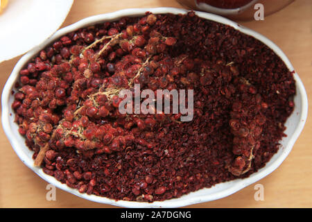 Getrocknete sumac Gewürz in eine hölzerne Schüssel, Ansicht von oben. eine Handvoll roter Sumach Pulver in einer Platte abstrakt Hintergrund. Sumak Körner und Pulver. Sumac ist in Stockfoto